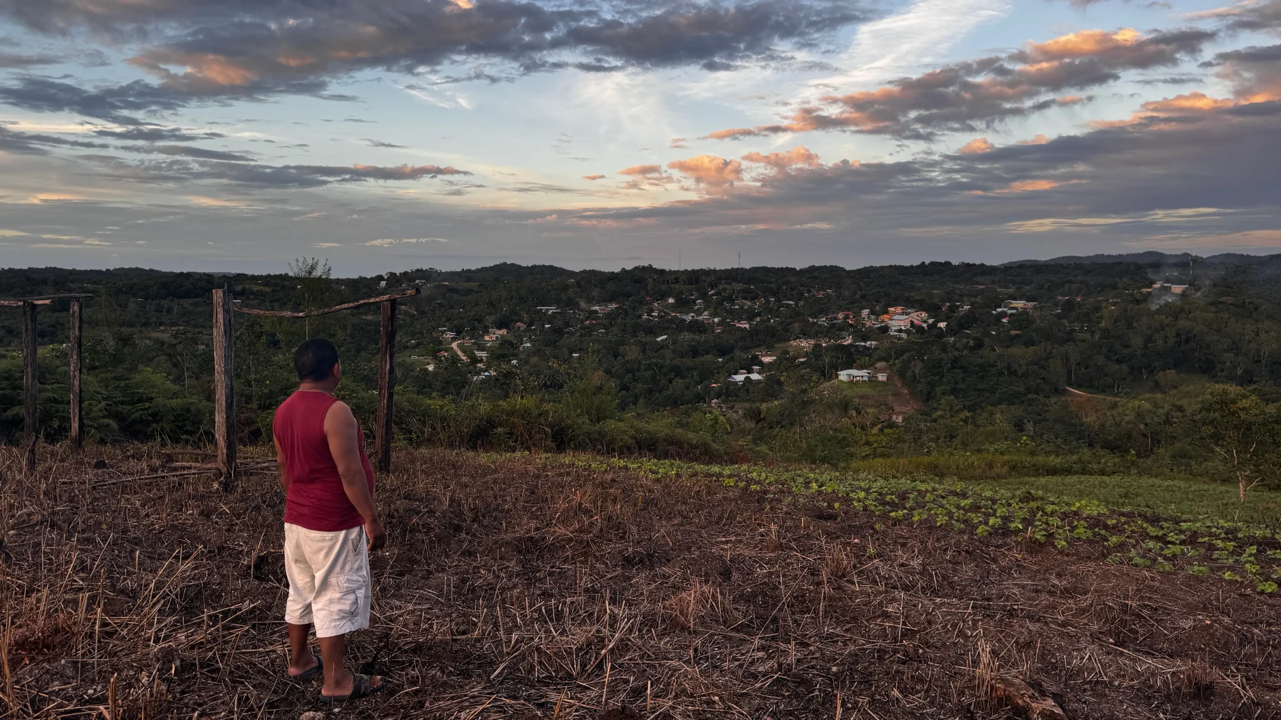 Man standing on hilltop land overlooking San Antonio village, Cayo District Belize at sunset